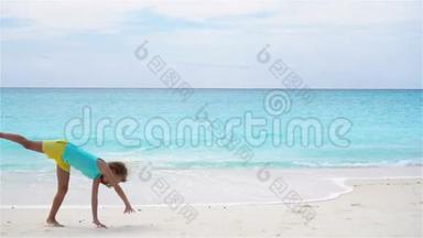 活跃的小女孩在海滩上玩得很开心。 运动的孩子在海岸上做轮子的慢动作